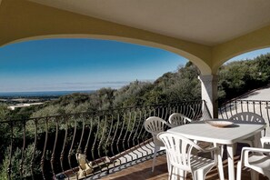 A balcony with white chairs and a table, overlooking a scenic landscape with trees and a distant view. - Spacious Beach Apartment for 6 (Badesi)