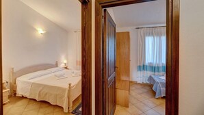 Ein Schlafzimmer mit Bett, Nachttischen, einer zur nächsten Kammer führenden Tür und einem mit Vorhängen versehenen Fenster.