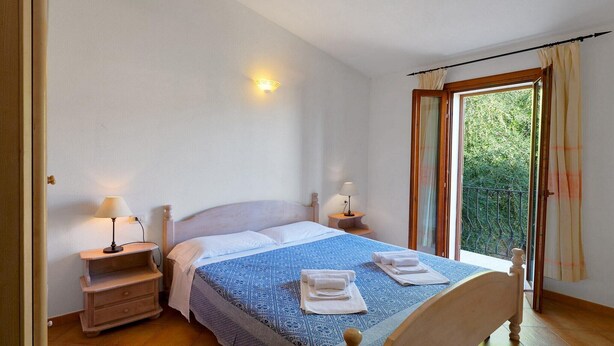 Un dormitorio con cama, dos mesitas de noche con lámparas, una ventana con cortinas y vistas al exterior.
