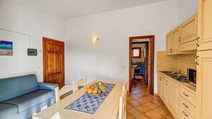 Un comedor con una mesa dispuesta para dos personas, un sofá azul y una cocina con armarios de madera y salpicadero de azulejos.