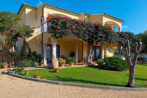 A two-story building with a balcony, potted plants, and a well-maintained lawn. - Chic Sardinian Escape by the Beach (Badesi)