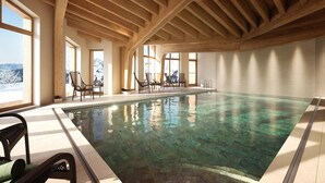 Piscina interior com vigas de madeira, água cristalina e vista para montanhas nevadas.