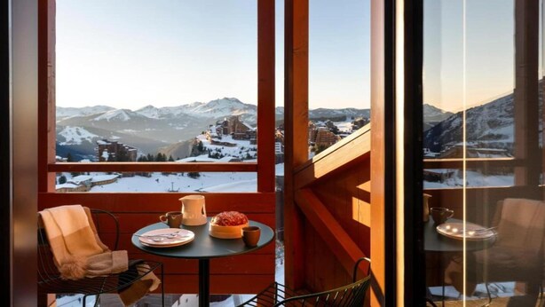 Varanda com mesa posta para dois, com vista para uma paisagem nevada de montanhas.