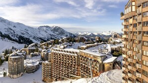 Uma cidade nas montanhas coberta de neve, com edifícios de vários andares, incluindo uma estrutura de madeira notável com sacadas.