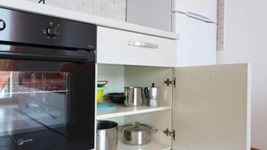 A kitchen with a black oven, white cabinets, and a shelf with pots and pans.