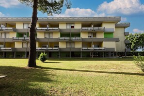 Un edificio a più piani con balconi, un tetto piatto e un cortile lastricato di erba.