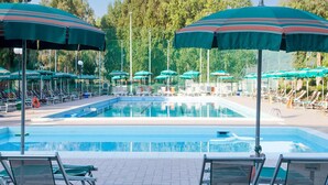 A swimming pool with multiple lounge chairs and umbrellas, surrounded by trees.