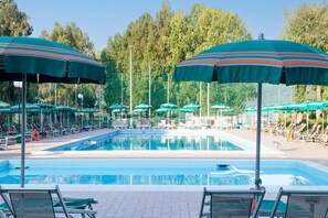 Una piscina con numerosi lettini e ombrelloni, circondata da alberi.