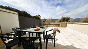 An outdoor patio with a table and chairs, a glass of orange juice, and a view of the countryside.
