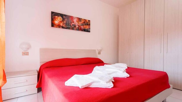 A bedroom with a bed, a white nightstand, a white wardrobe, and a wall-mounted light fixture.