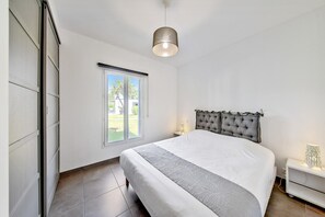 Et soveværelse med seng, vindue, natbord og lampe.