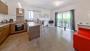 Een moderne keuken met een centraal eiland, een eethoek met tafel en stoelen, een rode bank en een groot raam met gordijnen.