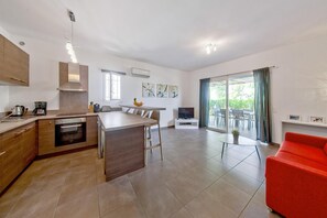 Eine moderne Küche mit einer zentralen Kochinsel, einem Essbereich mit Tisch und Stühlen, einem roten Sofa und einem großen Fenster mit Vorhängen.