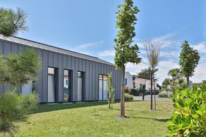 Ein modernes Gebäude mit flachem Dach, großen Fenstern und einem gepflegten Rasen mit jungen Bäumen.