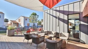 Eine moderne Außenpatio mit Korbmöbeln, einem großen Topfblumen und einer Glastür zu einem Innenbereich.
