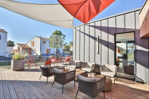 Eine moderne Außenpatio mit Korbmöbeln, einem großen Topfblumen und einer Glastür zu einem Innenbereich.