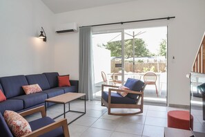 Ein modernes Wohnzimmer mit einer Couch, Sesseln, einem Couchtisch und einer Glastür, die zu einem Außenbereich führt.