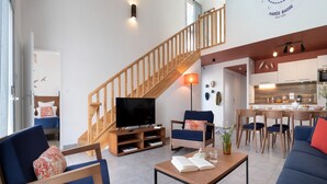 Ein modernes Wohnzimmer mit Fernseher, Sofa, Couchtisch und einer Treppe, die in eine Küche führt.