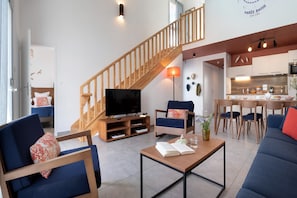 Ein modernes Wohnzimmer mit Fernseher, Sofa, Couchtisch und einer Treppe, die in eine Küche führt.