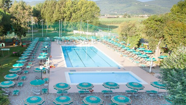Piscina com espreguiçadeiras e guarda-sóis, cercada por árvores e vista para colinas.
