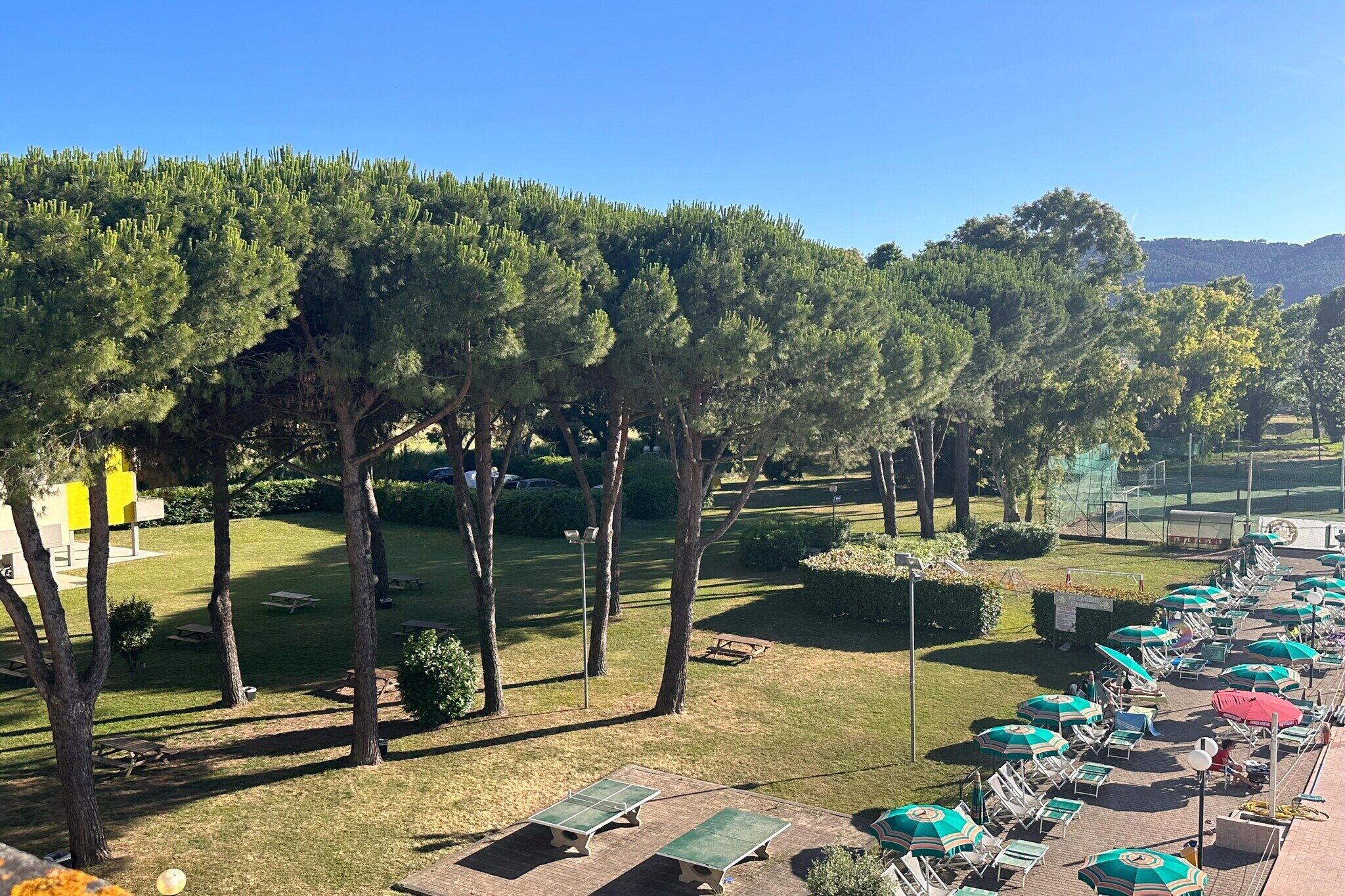 Un cortile con posti a sedere all'aperto, un campo da tennis e una fila di ombrelloni.