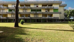 Um edifício de vários andares com varandas, um telhado plano e um pátio ajardinado.