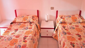 Quarto duplo com duas camas, cada uma com colcha de padrão floral, mesa de cabeceira com abajur branco e cabeceira vermelha.