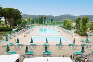 Area piscina con lettini e ombrelloni, circondata da alberi e colline.