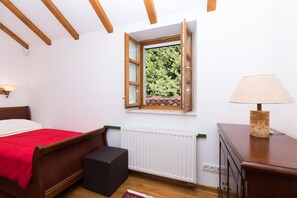 Une chambre à coucher comprenant un lit, une petite table, une lampe, un radiateur et une fenêtre donnant sur des arbres.