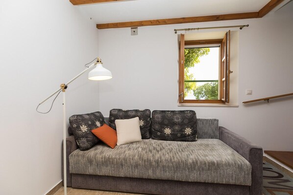 Un canapé gris agrémenté de coussins à motifs floraux, un lampadaire blanc et une fenêtre avec un cadre en bois.