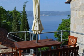 Ein Balkon mit Tisch und Stühlen, mit Blick auf ein Gewässer und entfernte Küsten.