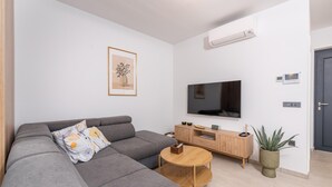A modern living room with a grey sofa, a wooden coffee table, a TV, and a potted plant. - 6-Person Home with 3 En-Suites (Novigrad)