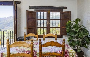 Ein Schlafzimmer mit Bett, einem Fenster mit Rollläden, einer Topfpflanze und Blick auf Berge.
