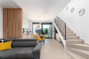 Ein modernes Wohnzimmer mit Sofa, Essbereich, Treppe und Küche.