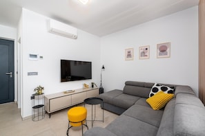 A modern living room with a grey sofa, a flat-screen TV, a small side table, a yellow ottoman, and a wall-mounted air conditioner. - Detached Holiday Villa for 6 (Novigrad)