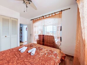 A bedroom with a bed, a ceiling fan, a window with a sheer curtain, and a door with louvered panels. - Hameau la Madrague by Interhome (Saint Cyr sur Mer La Madrague)