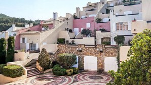 Uma vila em encosta com edifícios de pedra tradicionais, telhados em terraço e um pátio circular em mosaico.