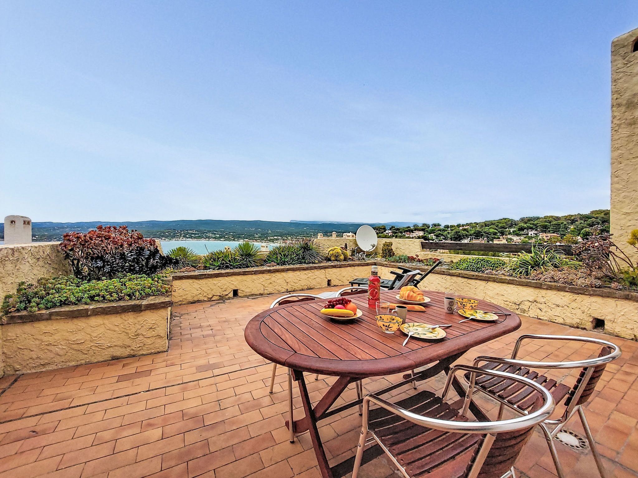 Une terrasse avec une table et des chaises, une antenne parabolique et une vue sur la mer et les collines.