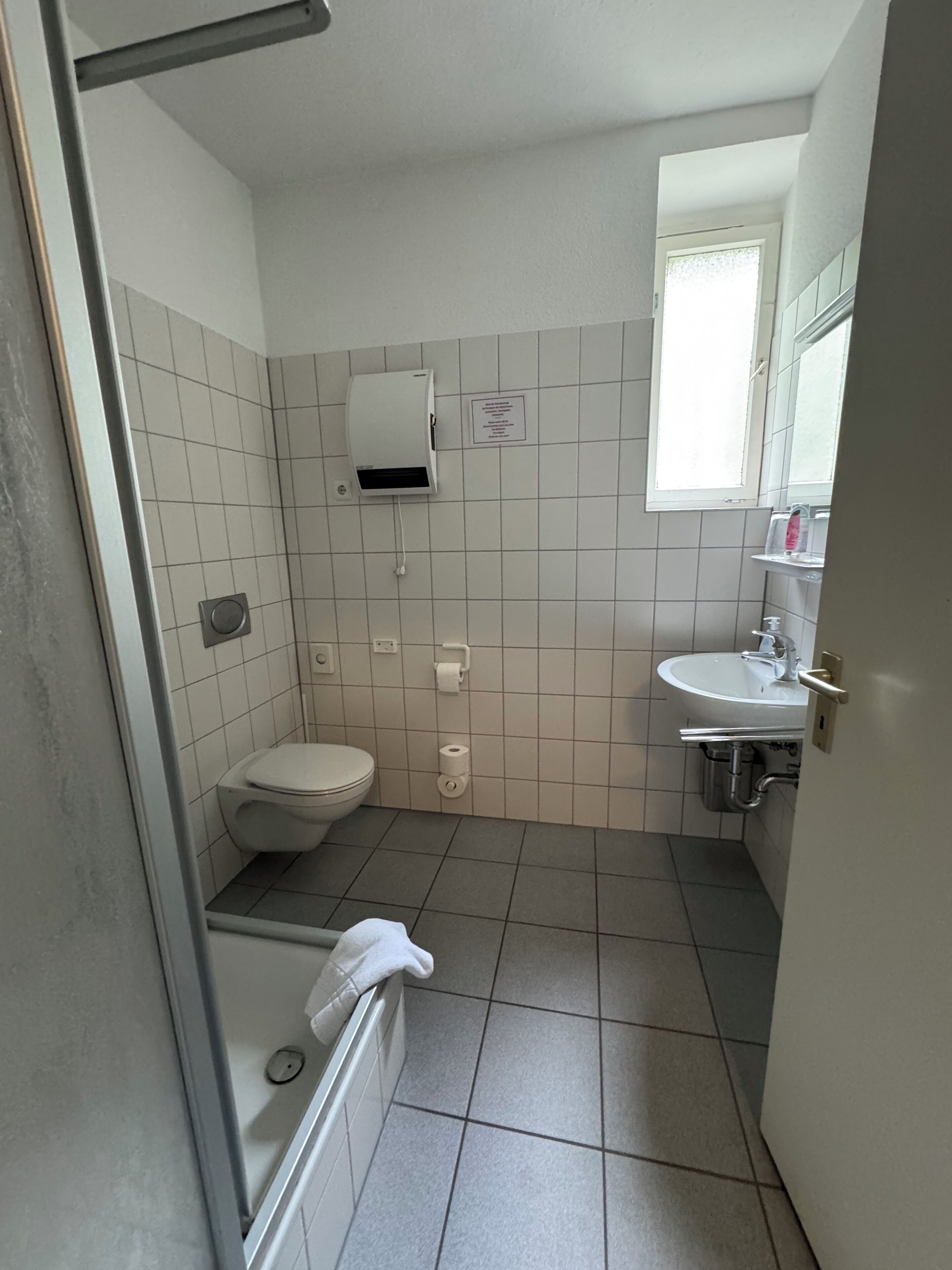 Un baño pequeño con azulejos, que incluye un inodoro, un lavabo, un secador de manos y un perchero para toallas.