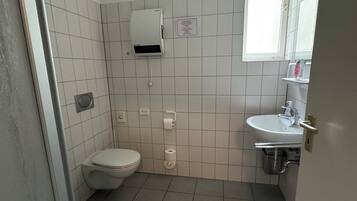 Un baño pequeño con azulejos, que incluye un inodoro, un lavabo, un secador de manos y un perchero para toallas.