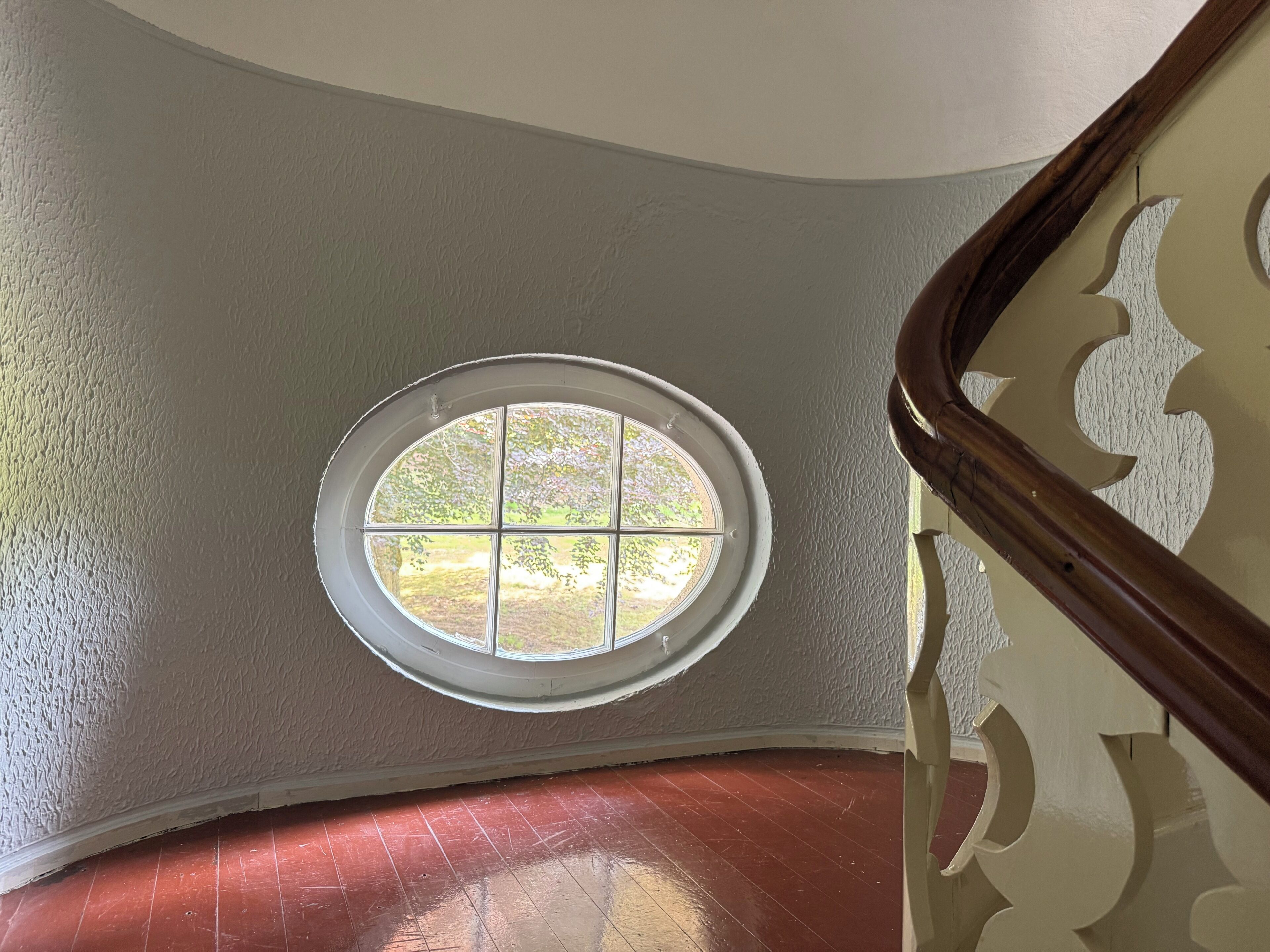 Een trap met een rond raam in de muur, een houten leuning en een structuurrijke wand.