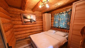 A log cabin bedroom with a bed, a window with curtains, a door, and a framed picture on the wall.