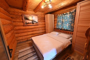 A log cabin bedroom with a bed, a framed picture on the wall, and a window with curtains.