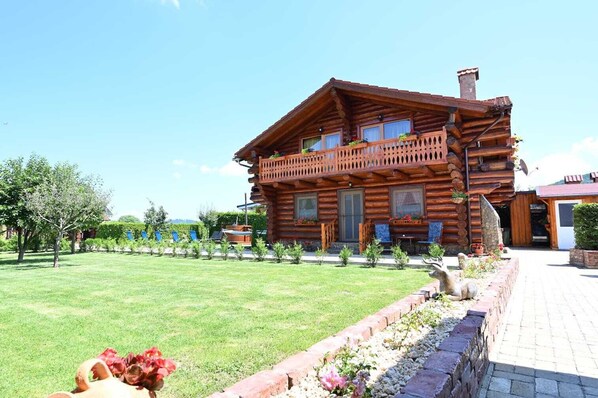 A log cabin with a balcony, a lawn, and a brick pathway.