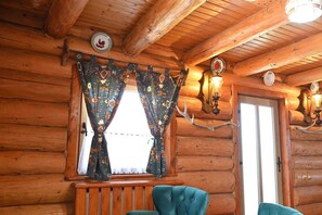 A log cabin interior with a window, curtains, a bench, and wall-mounted lights.