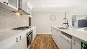 Una cocina moderna con armarios blancos, estufa a gas, lavavajillas y ventana con vistas al exterior.