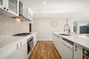 Uma cozinha moderna com armários brancos, fogão a gás, lava-louças e uma janela com vista para o exterior.