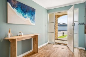 Um corredor com uma mesa consola de madeira, um quadro abstrato grande e uma porta de vidro que dá para o exterior.