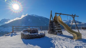 A snowy outdoor area with a wooden fence, a stone bench, and a wooden slide. - Ski Apartment with panoramic views (Mittersill)
