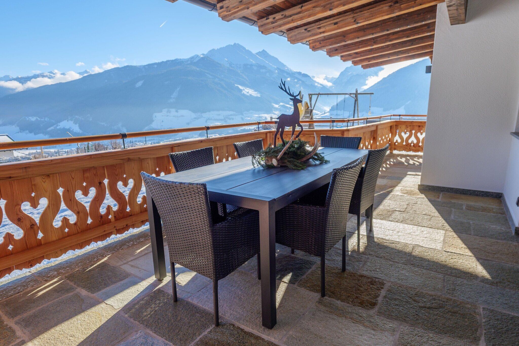 Varanda com mesa e cadeiras, um veado decorativo e vista para as montanhas.